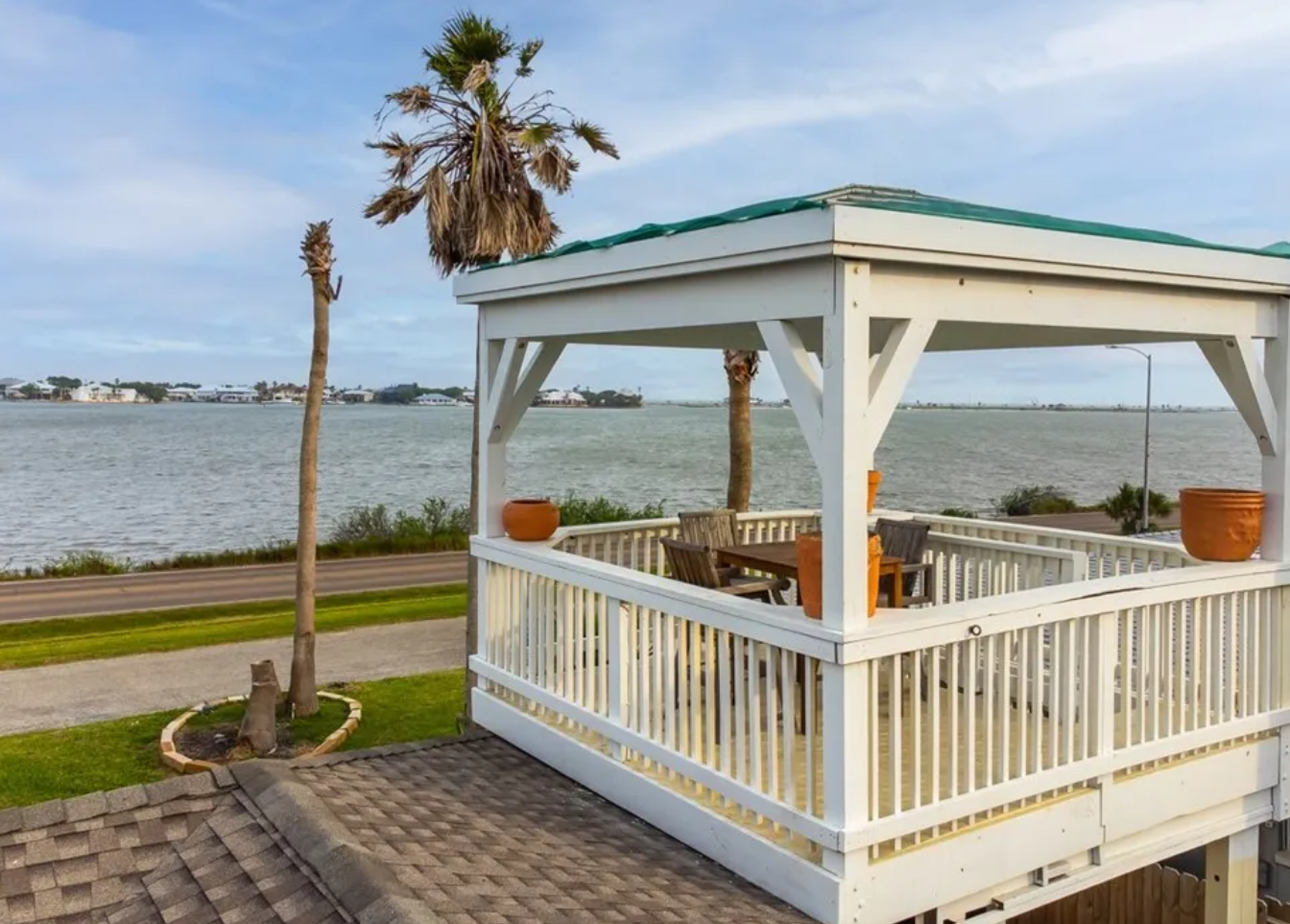 White gazebo overlooking water with palm trees; table and chairs inside.