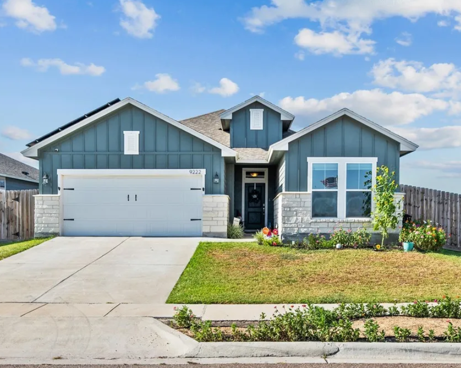 Blue house with stone accents, white garage door, and green lawn under a blue sky.