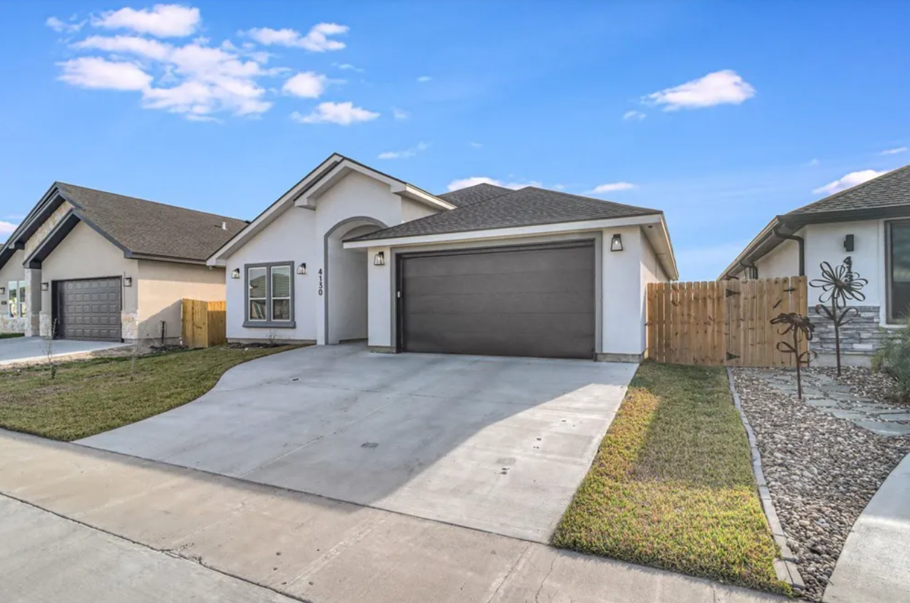 A white suburban house with a grey garage door and driveway, sunny day.