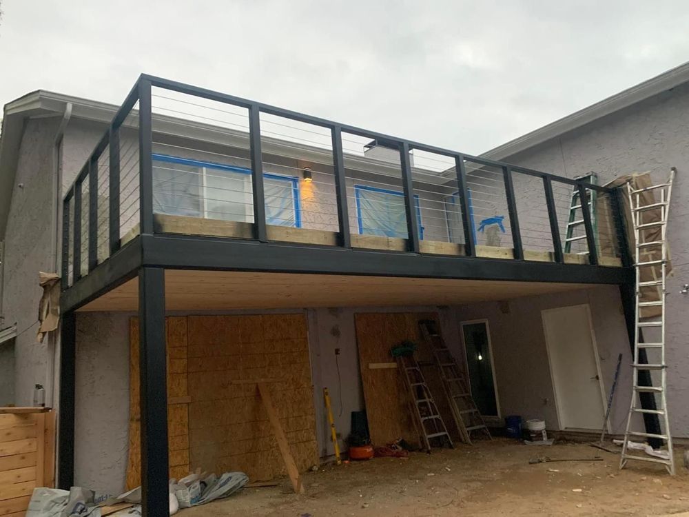 A two-story deck being built with a black frame and wire railings attached to a house.