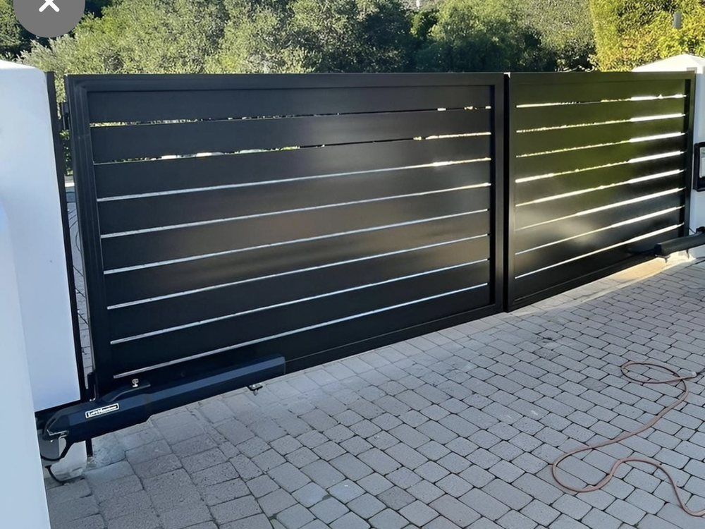 Black horizontal slat gate with automatic opener, on a brick driveway.