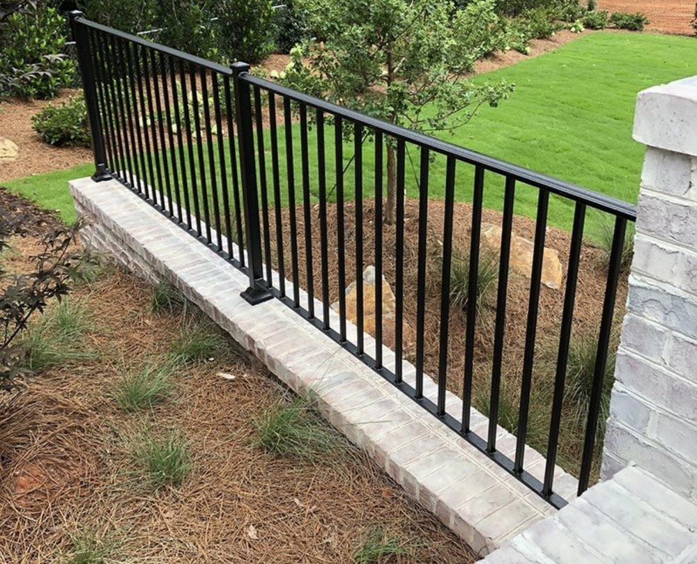 Black metal railing on a brick wall, beside grass.