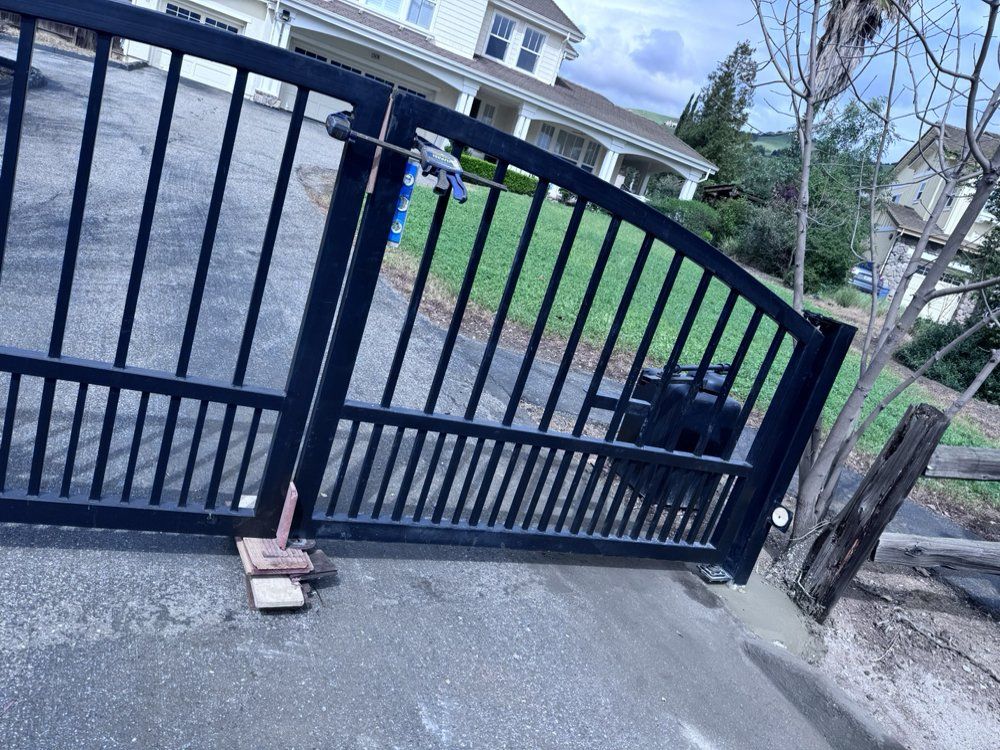 Black metal gate, slightly ajar, in front of a house with a green lawn.