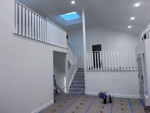 White interior with a staircase, loft, and skylight, freshly painted, awaiting flooring.