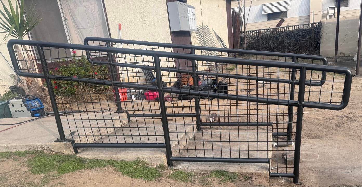 Black metal ramp with handrails, providing access over a small set of steps in a public outdoor area.