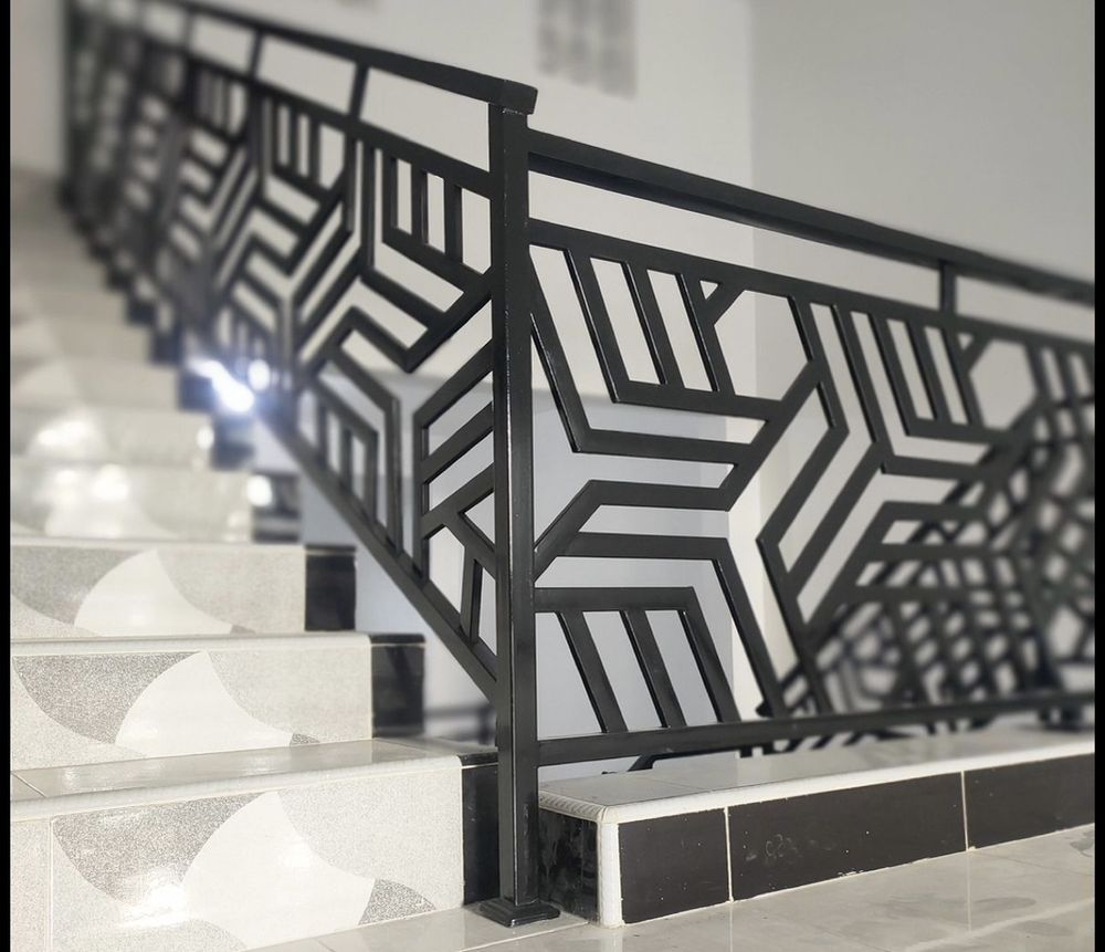Black metal stair railing with geometric starburst design. White and gray patterned stairs.