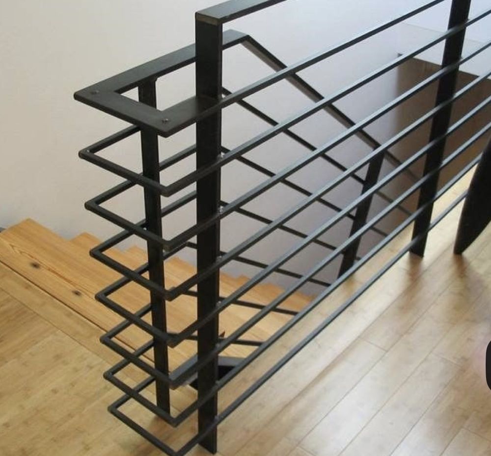 Black metal staircase railing with horizontal bars and a geometric design, next to wooden stairs and floors.