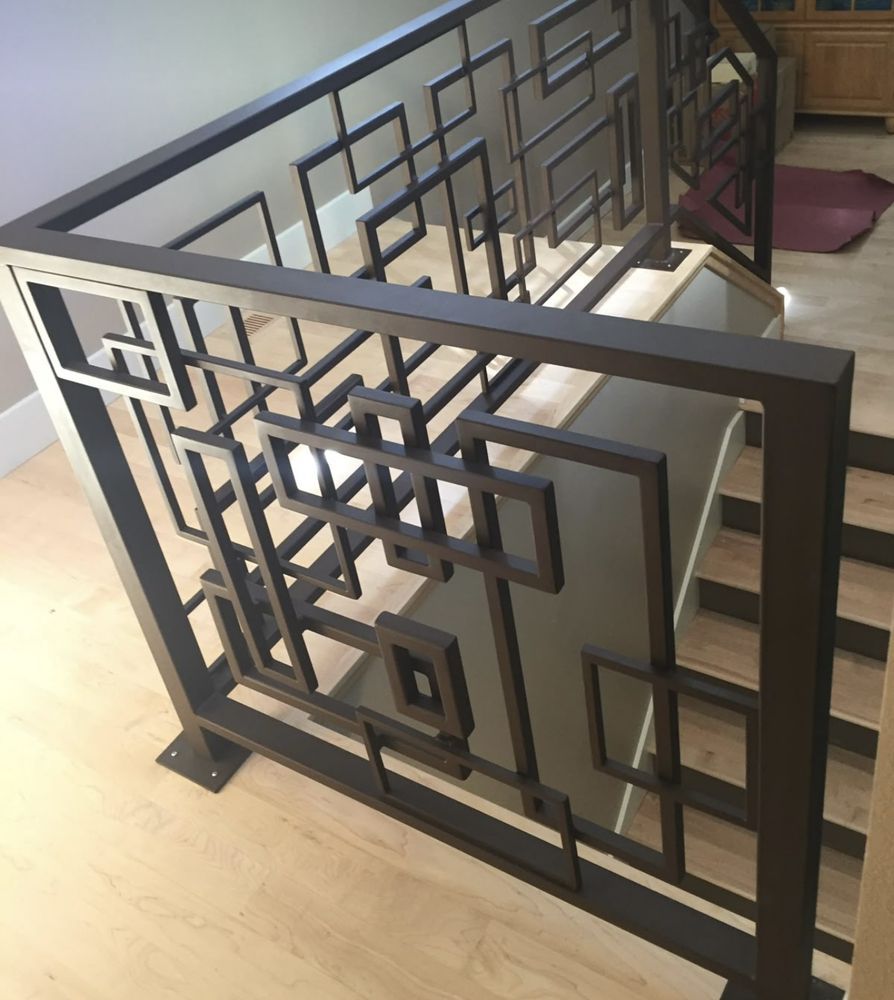 Geometric black metal railing on a light wood staircase.