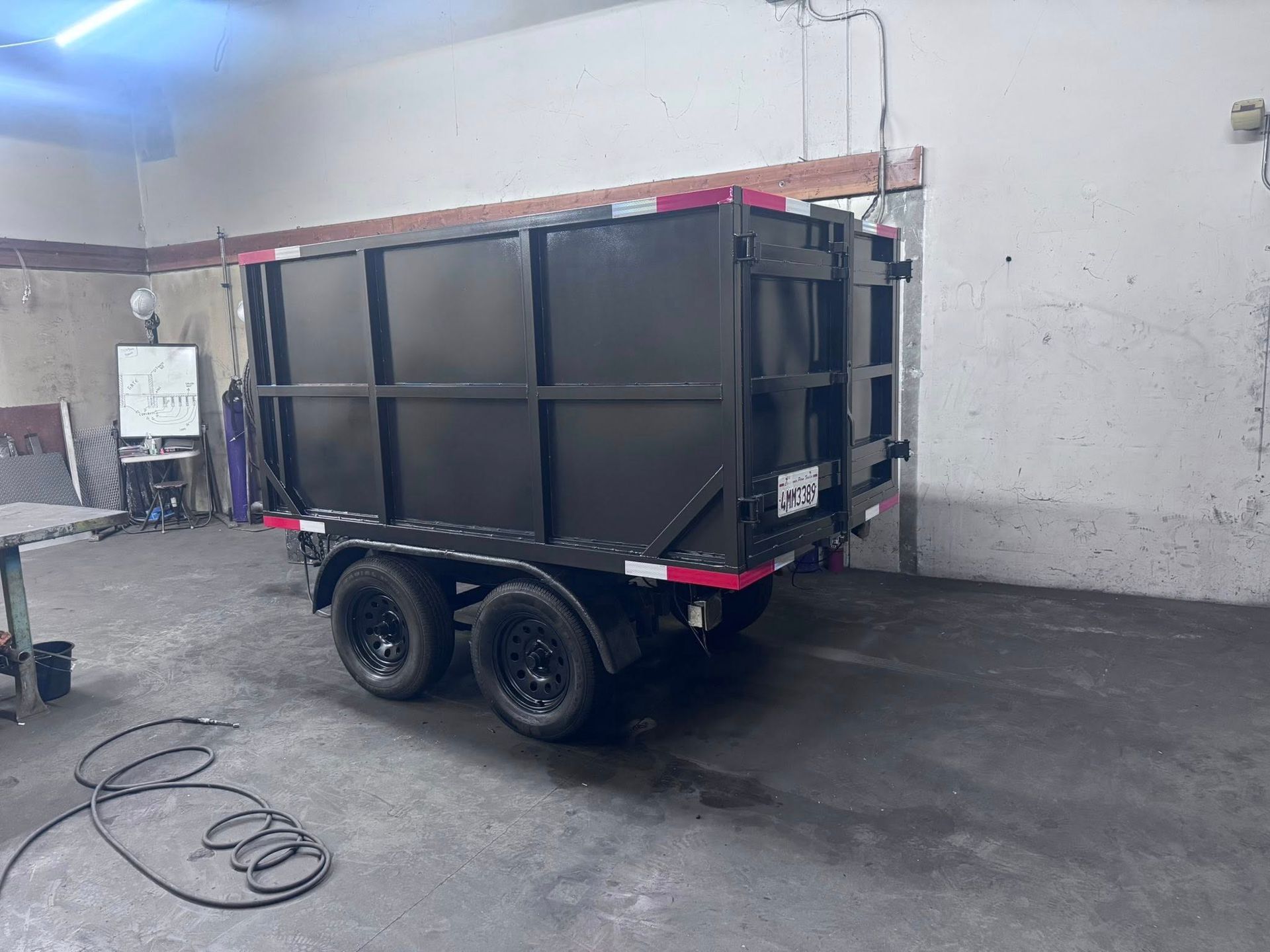 Black dump trailer with black wheels, red trim, indoors.