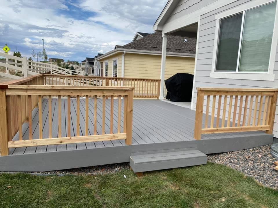 A gray deck with a wooden railing is in front of a house.