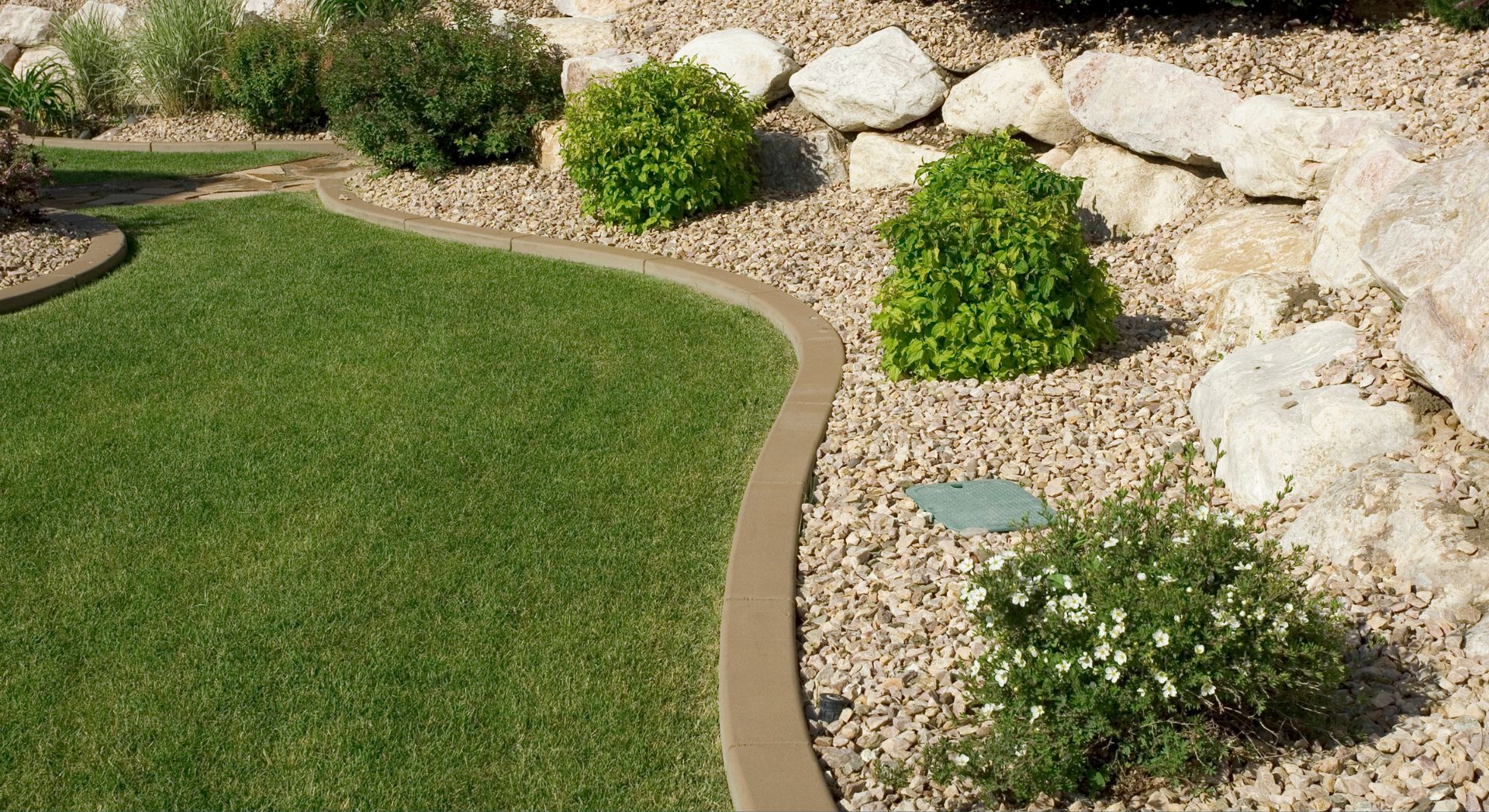 A lawn with a concrete curb and rocks in the background.
