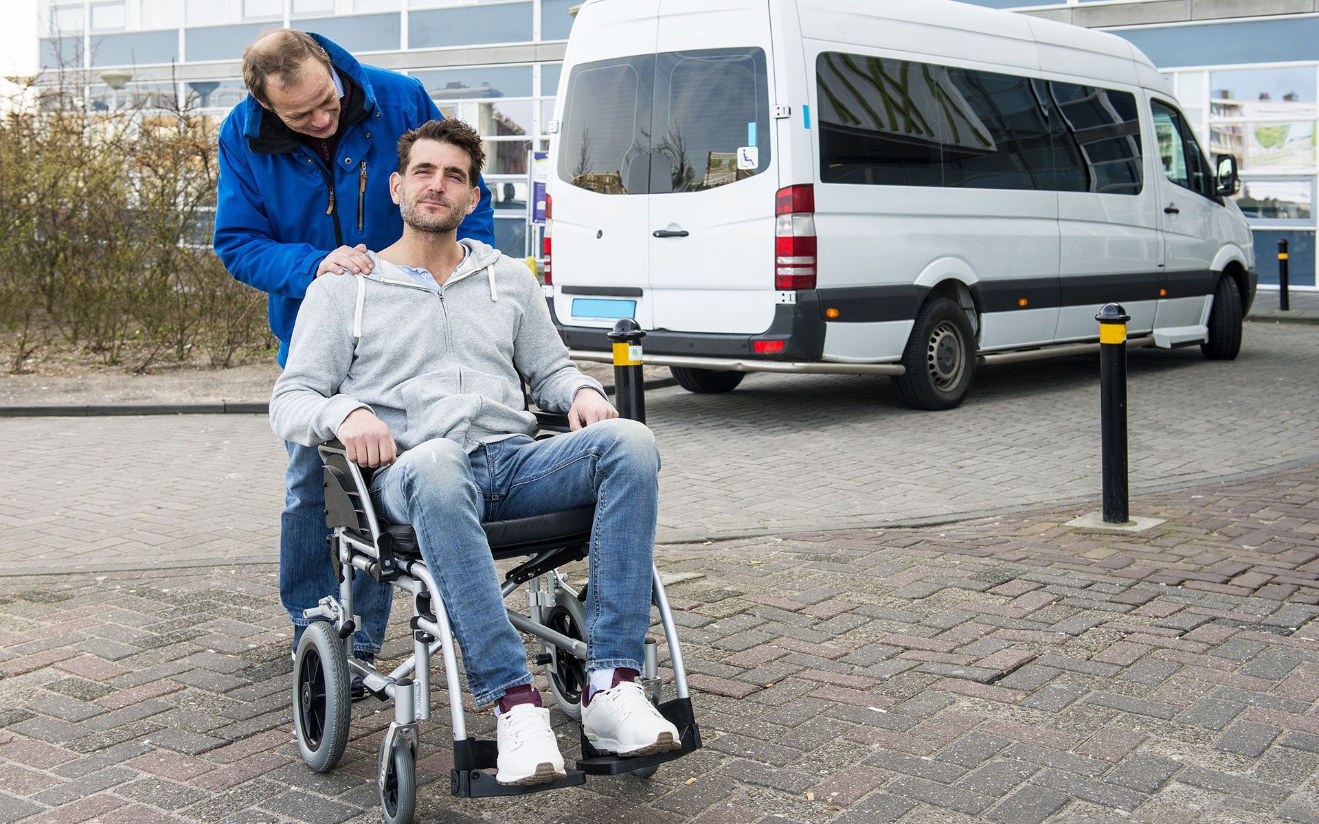 Man in wheelchair with assistant near a white van.