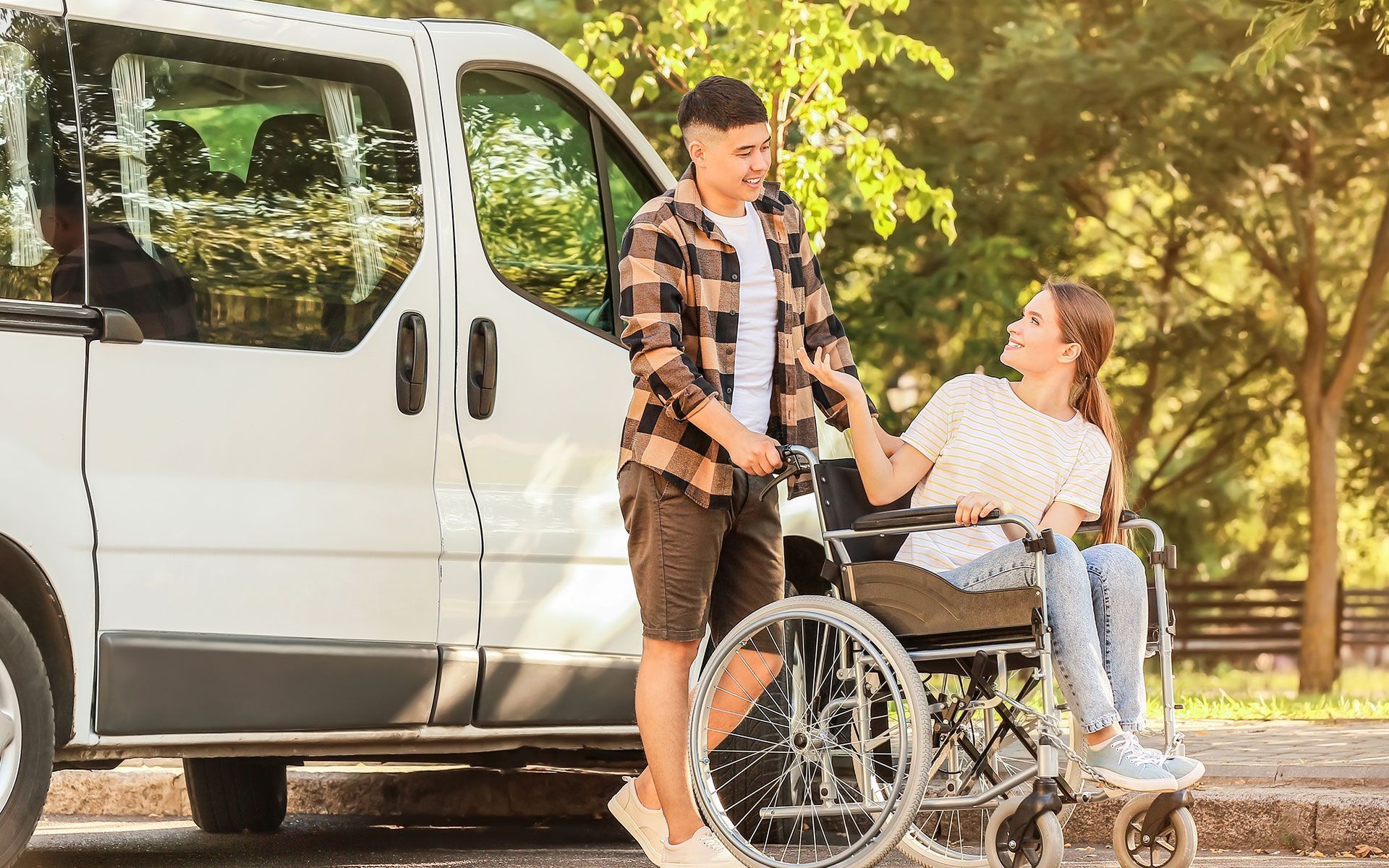 Man assisting woman in wheelchair near a white accessible van, outdoors.