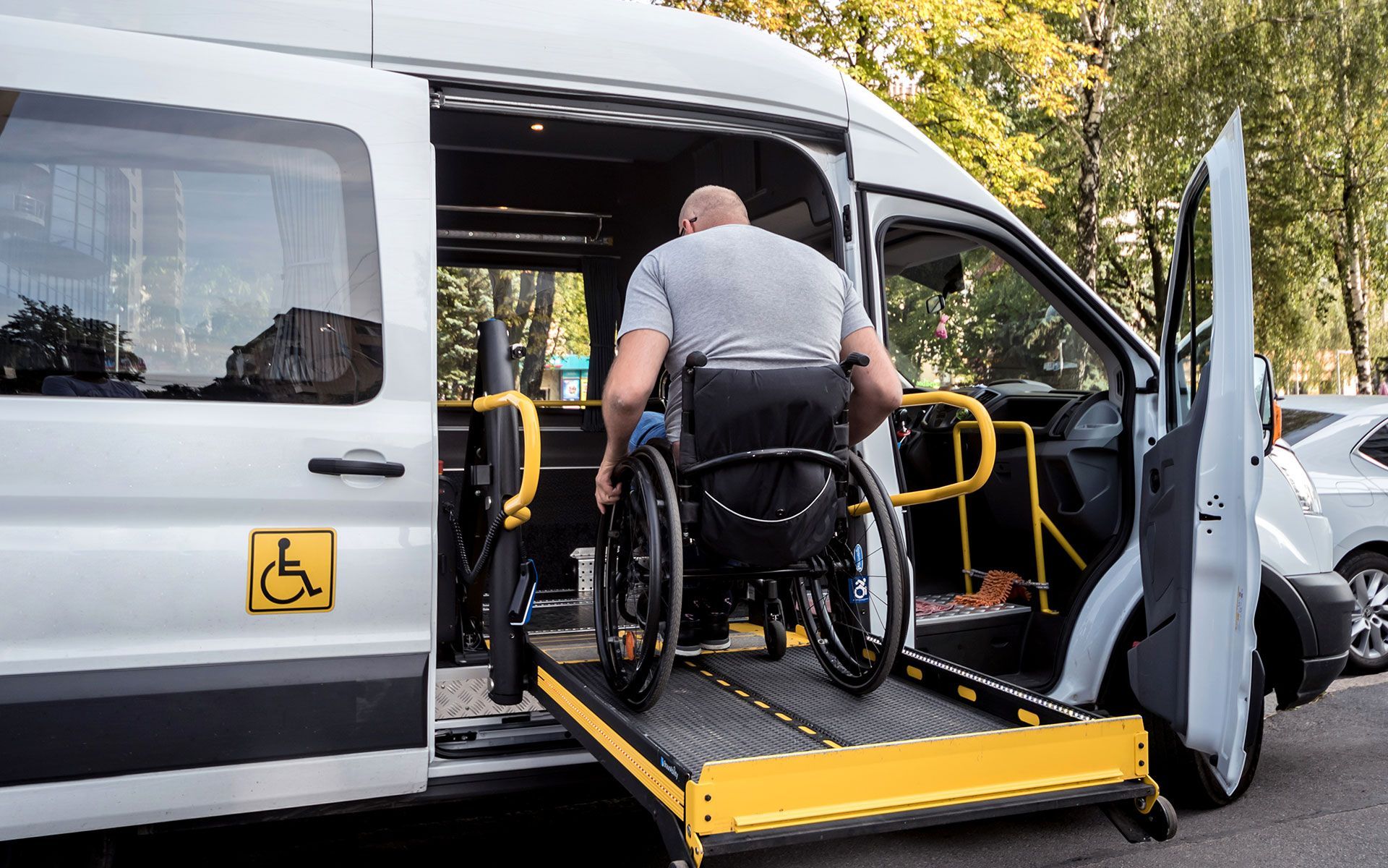 Man in wheelchair entering accessible van via ramp. Yellow handrails and ramp. Outdoor setting.