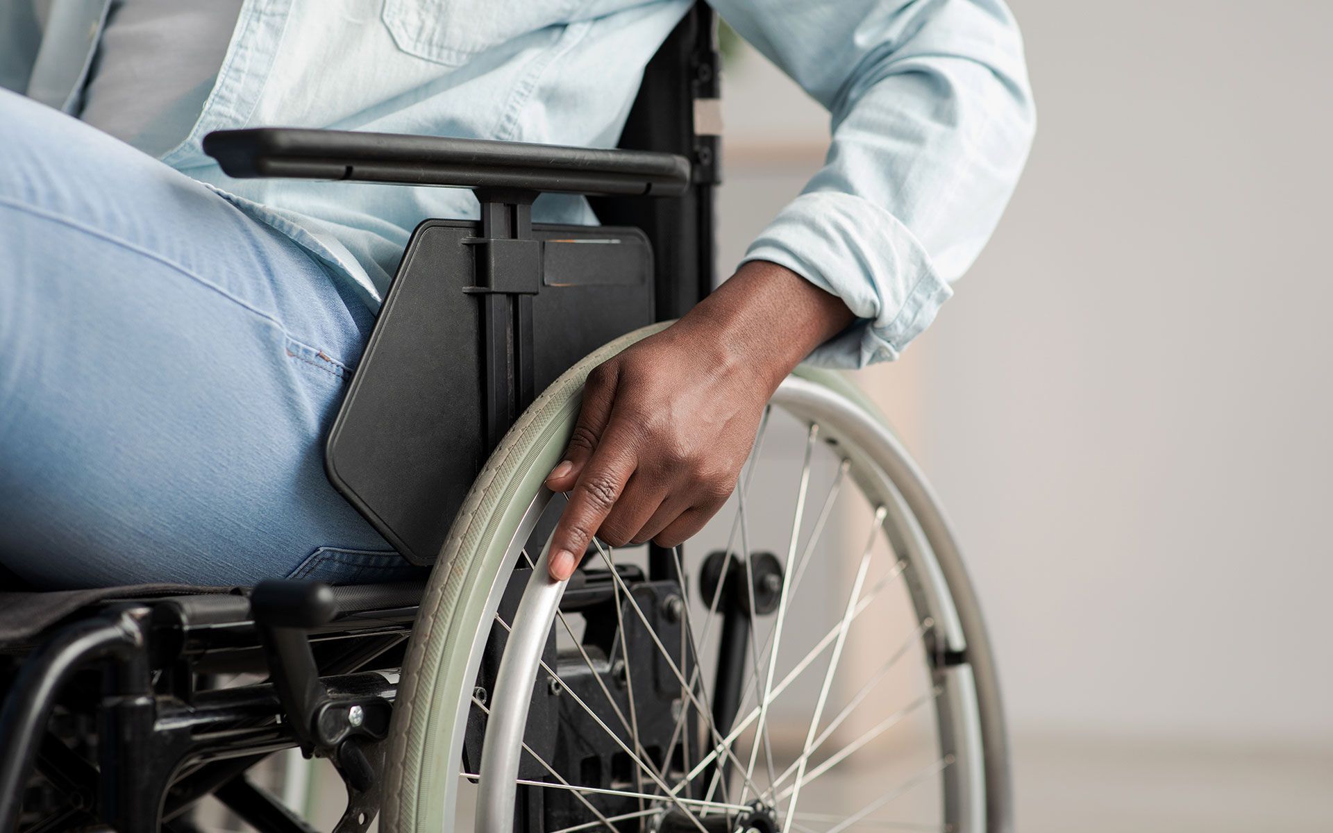 Person in wheelchair, hand resting on wheel, indoor setting.