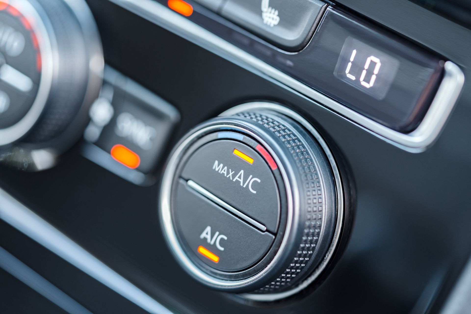 A close-up of a car's climate control dial with lit orange indicators for A/C and a digital display set to