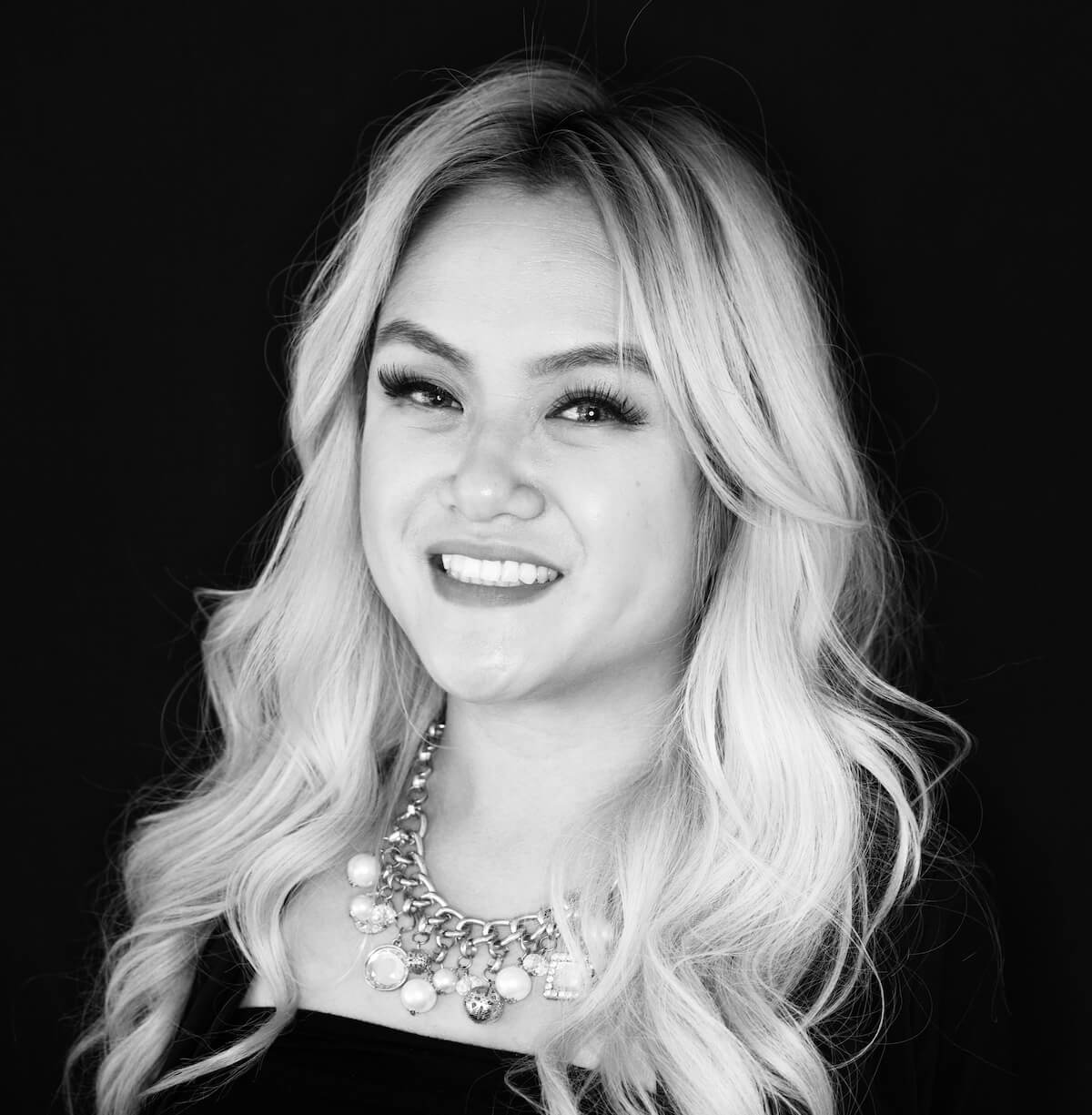 A black and white photo of a woman wearing a necklace and smiling.