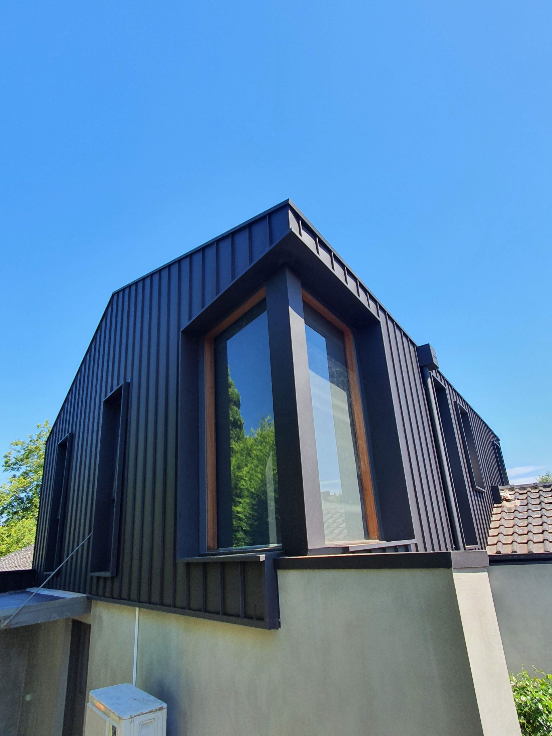 Black-paneled angular roof with large window, on a concrete foundation, against a bright blue sky.