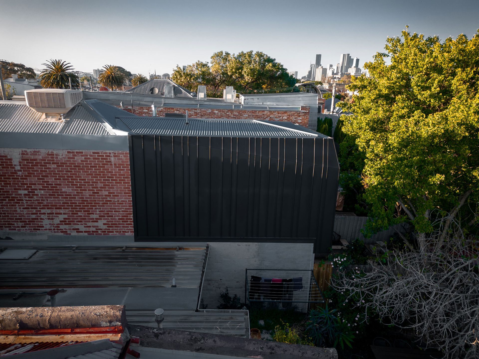 Rooftop view of buildings with a dark wall in the center and a city skyline in the distance.
