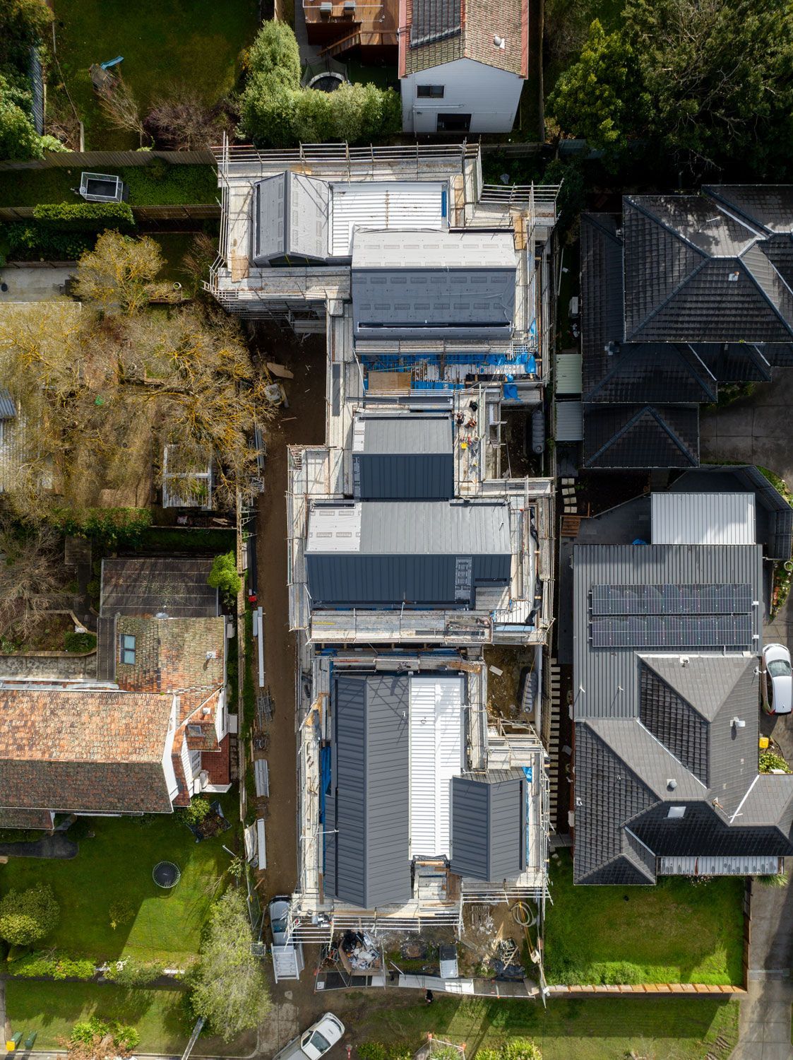 Aerial view of buildings under construction with flat dark gray roofs and solar panels.