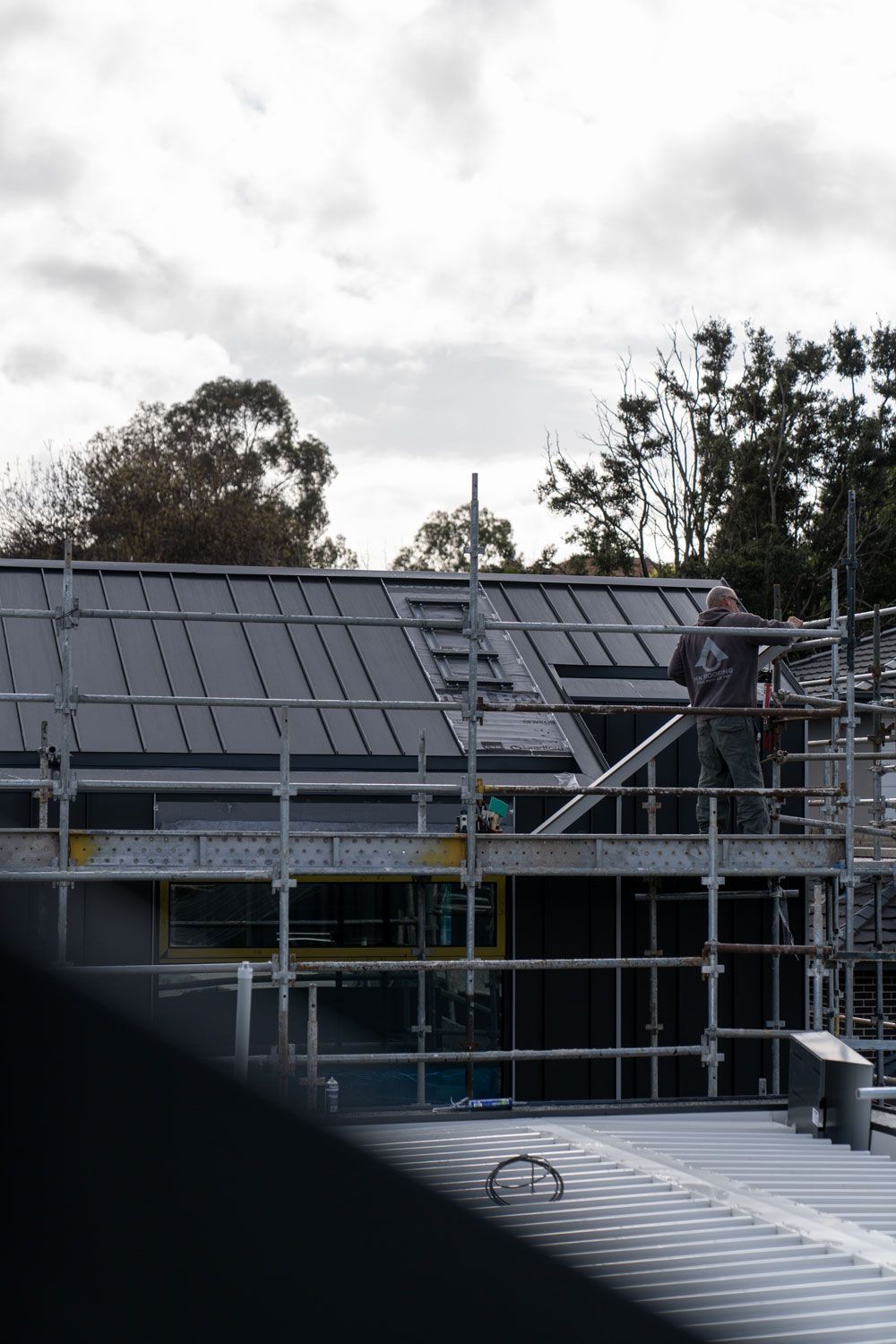 Construction worker on scaffolding installing dark gray roof panels.