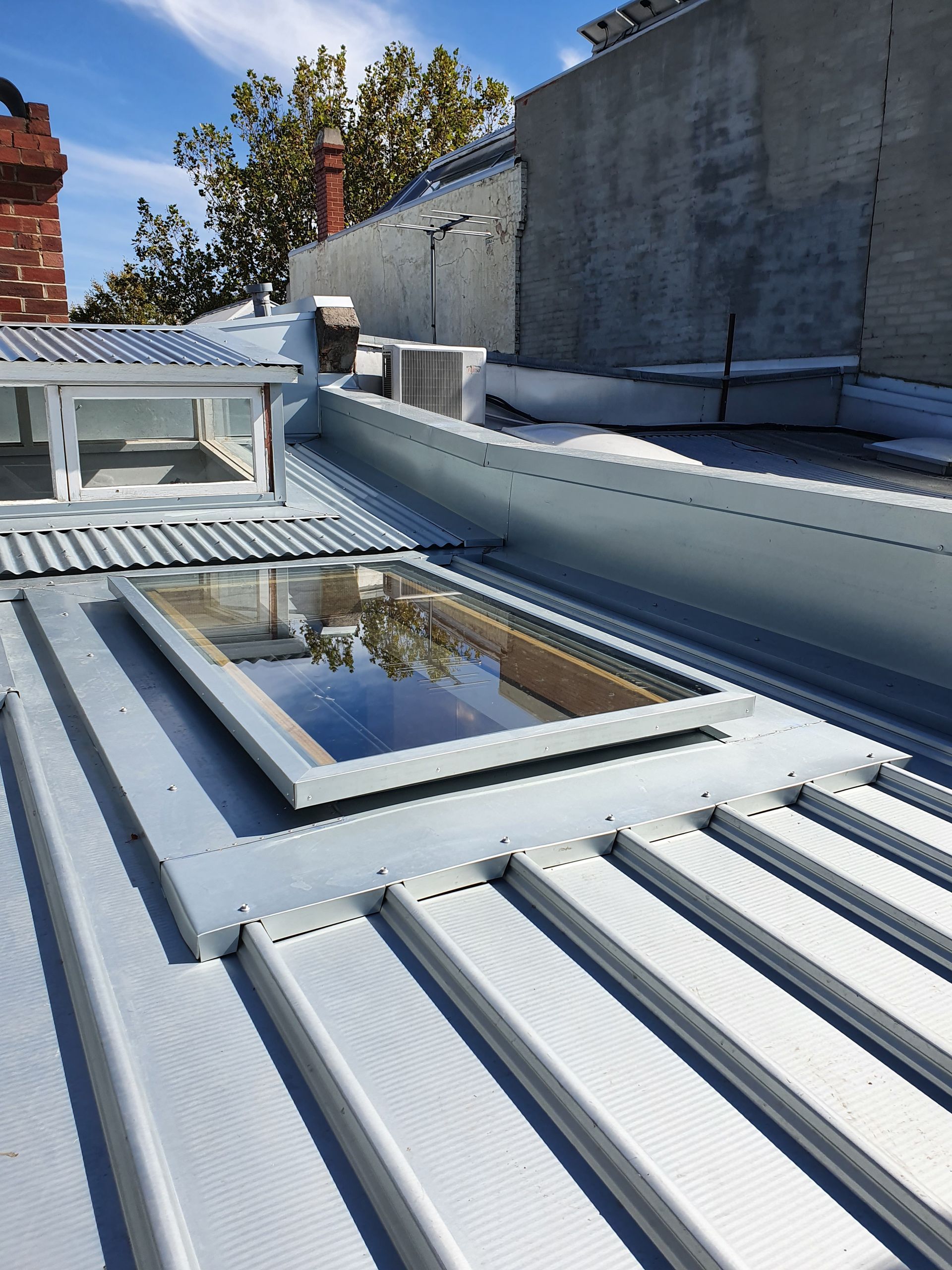 Rooftop with metal roofing, two skylights, and a vent. Blue sky.