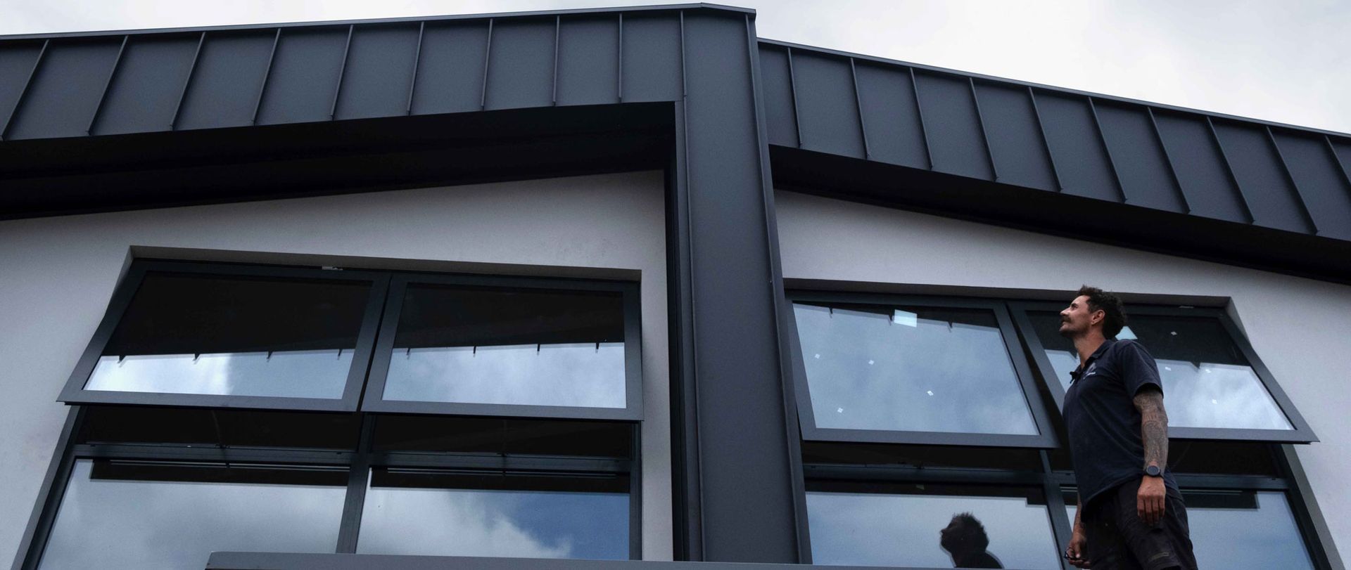 Man looking up at building with dark roof and open windows.