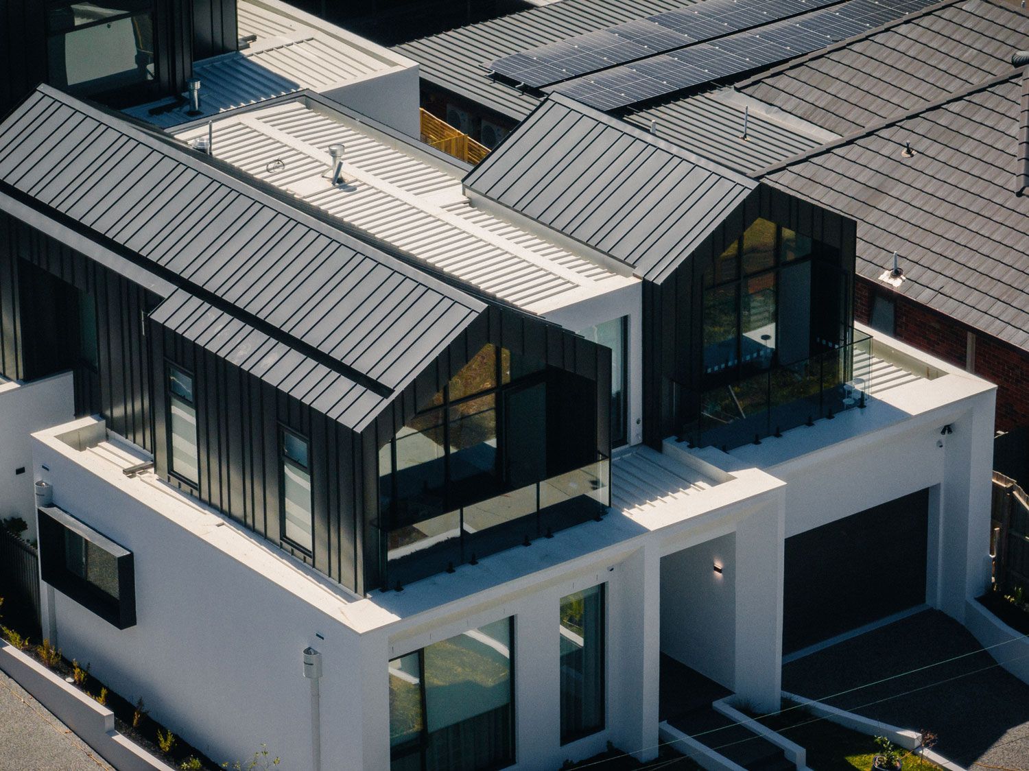 Modern house with black metal roof, white walls, and glass windows.