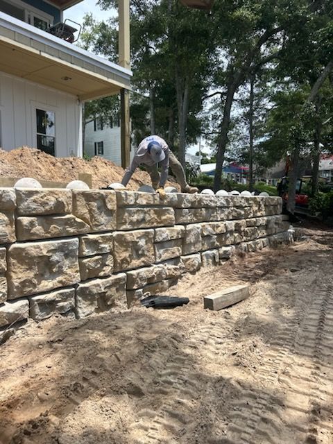 A man is working on a stone wall in front of a house.