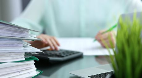 A person is sitting at a desk using a calculator and writing on a piece of paper.