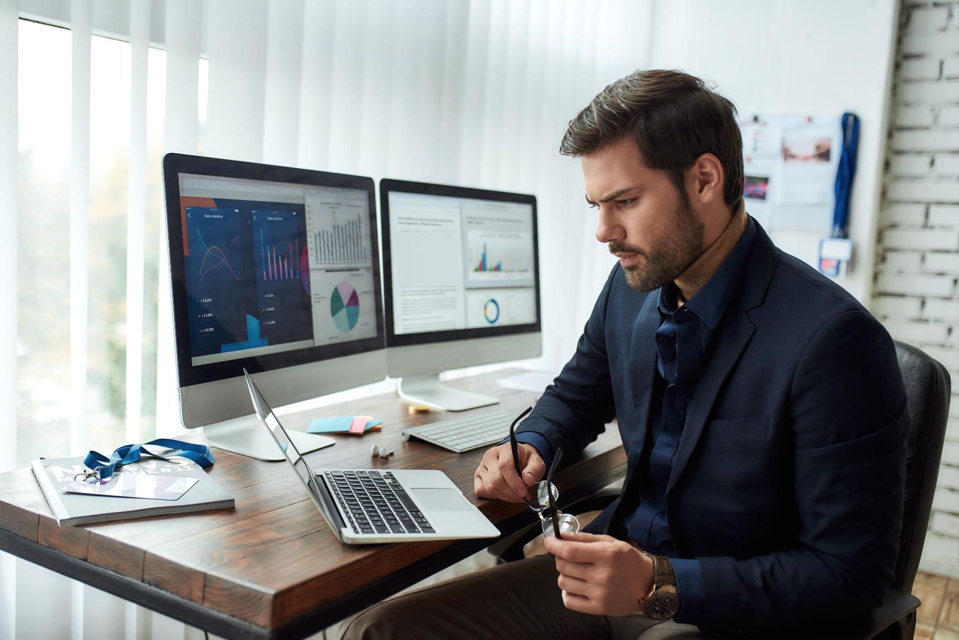A man is sitting at a desk with a laptop and two computer monitors.