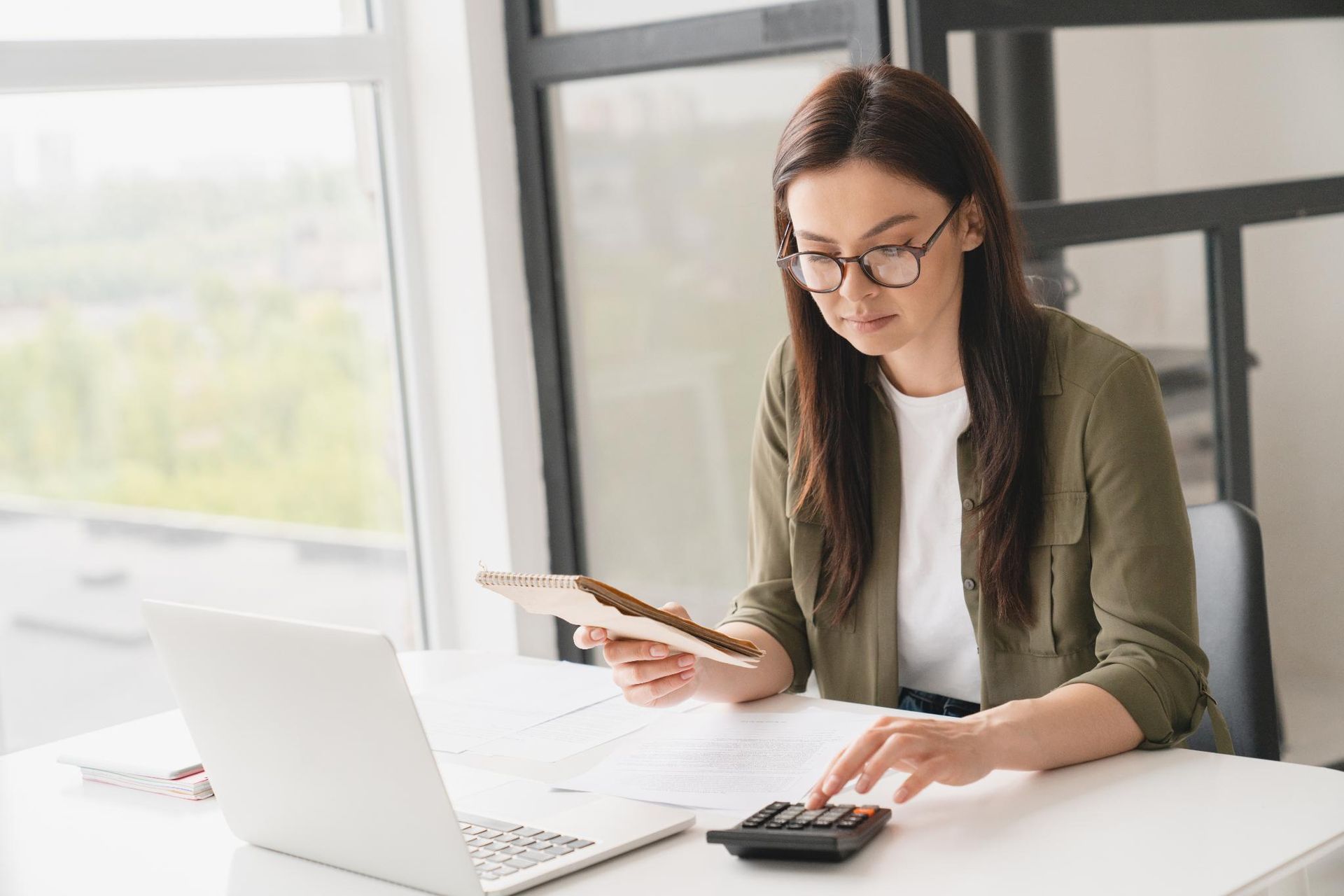 A woman is sitting at a desk with a laptop and a calculator.