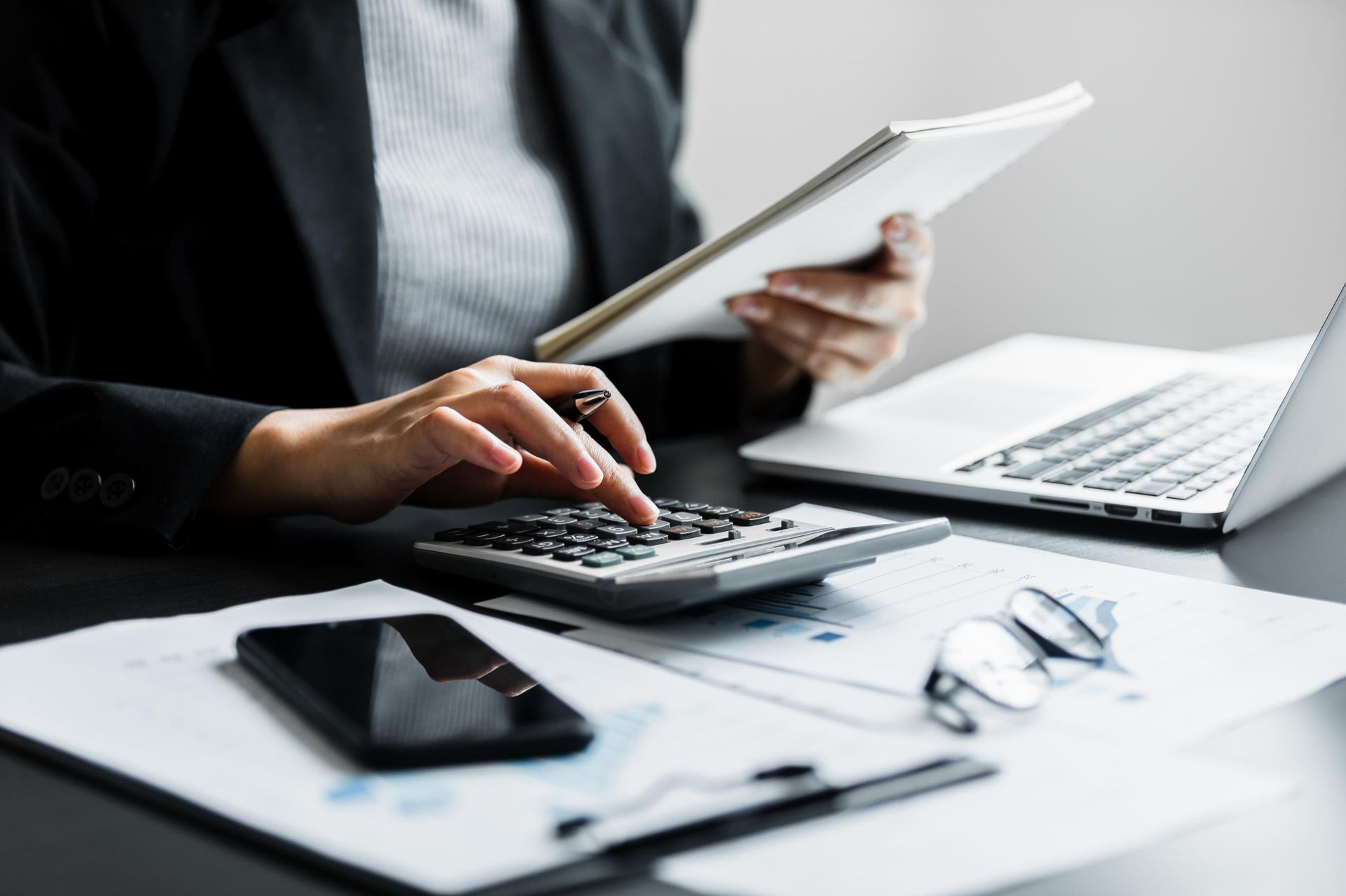 A woman is sitting at a desk using a calculator and a tablet.