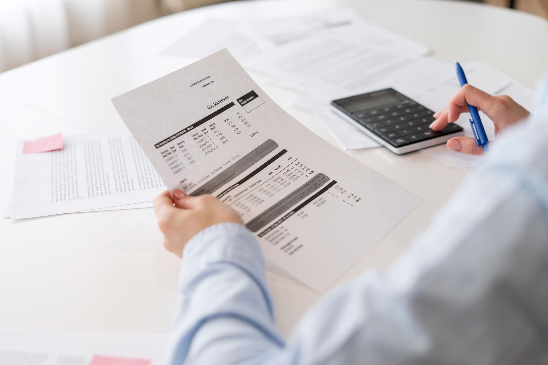 A person is sitting at a table holding a piece of paper and using a calculator.