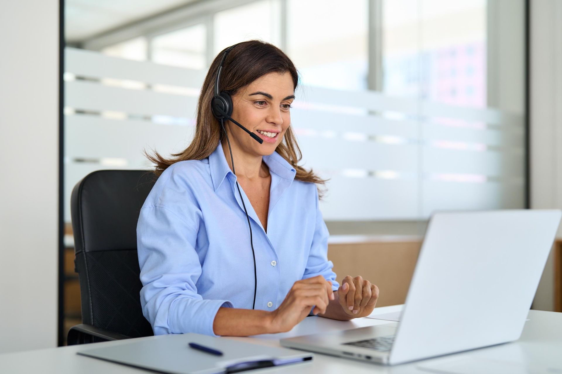 A woman wearing a headset is sitting in front of a laptop computer.