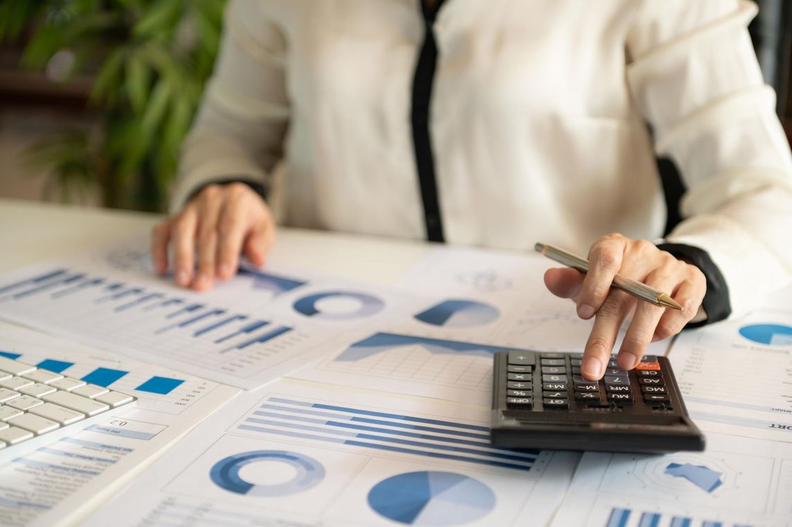 A woman is sitting at a table using a calculator and a pen.