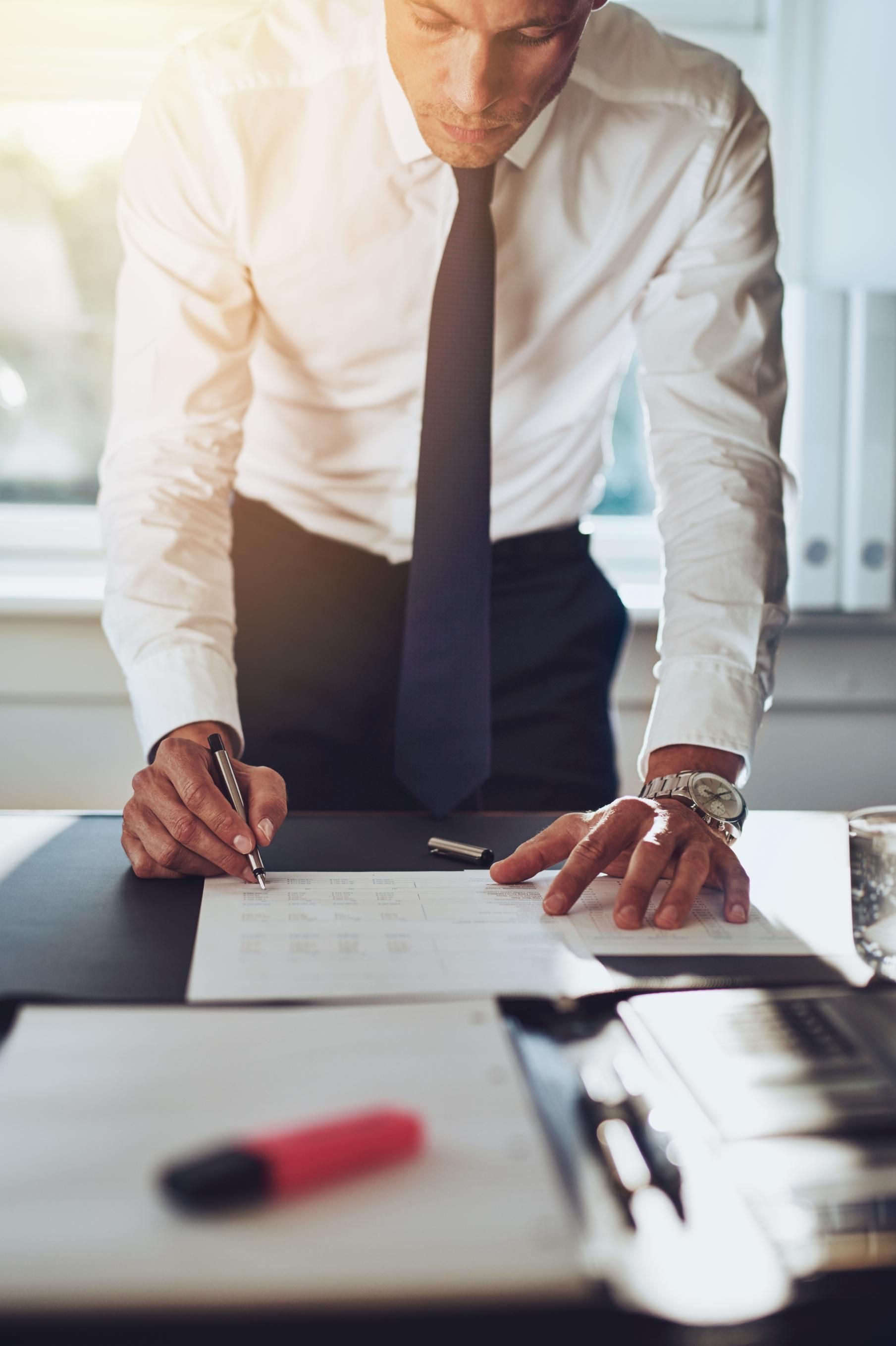 A man in a suit and tie is signing a document at a desk.