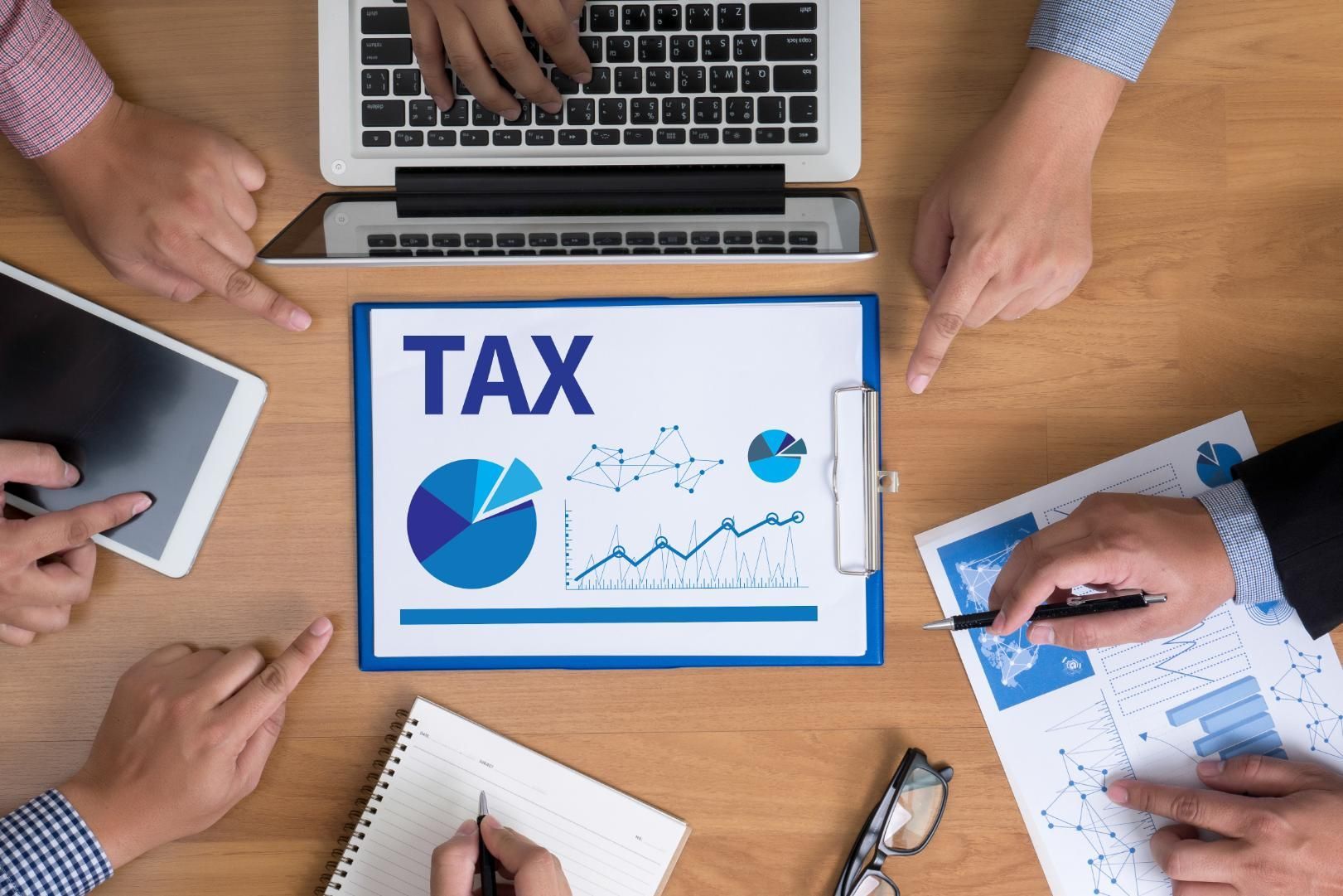 A group of people are sitting around a table looking at a clipboard with the word tax on it.
