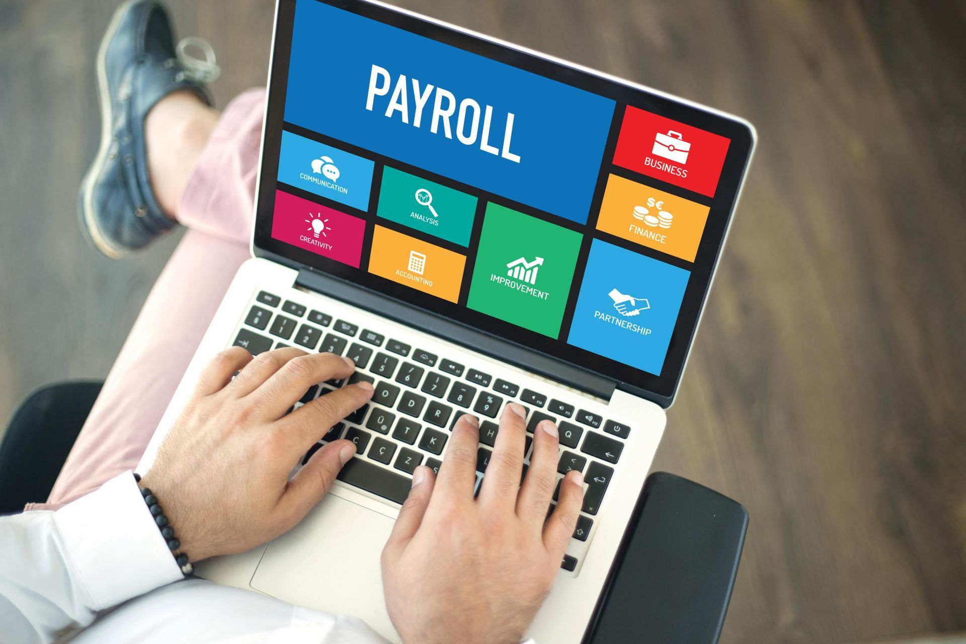 A person is typing on a laptop computer with the word payroll on the screen.