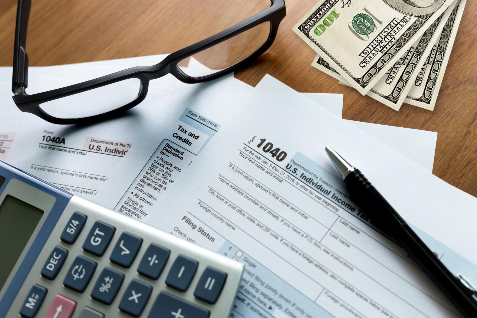 A 1040 tax form is on a table next to a pen and glasses.