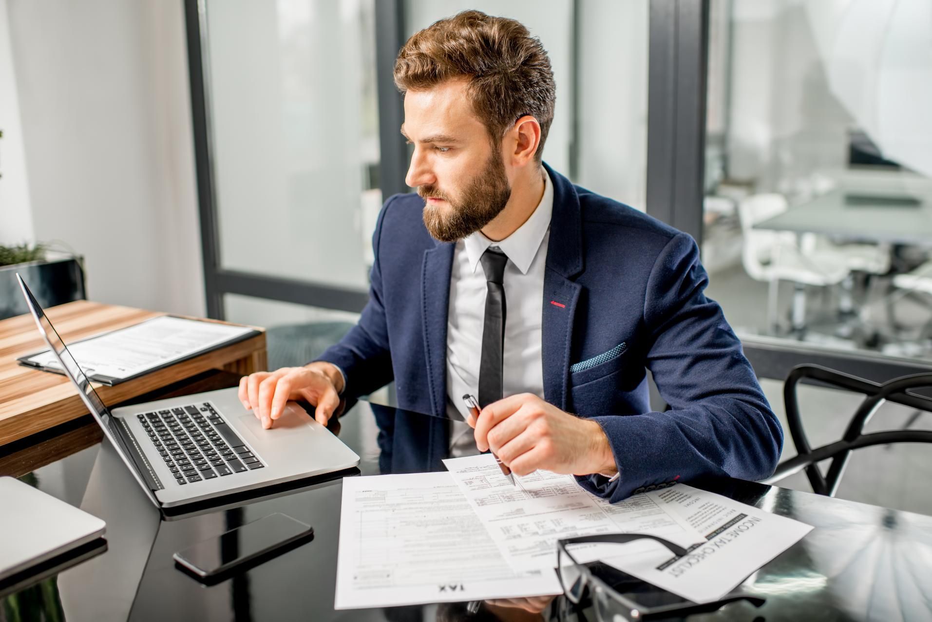 A man in a suit and tie is sitting at a desk using a laptop computer.