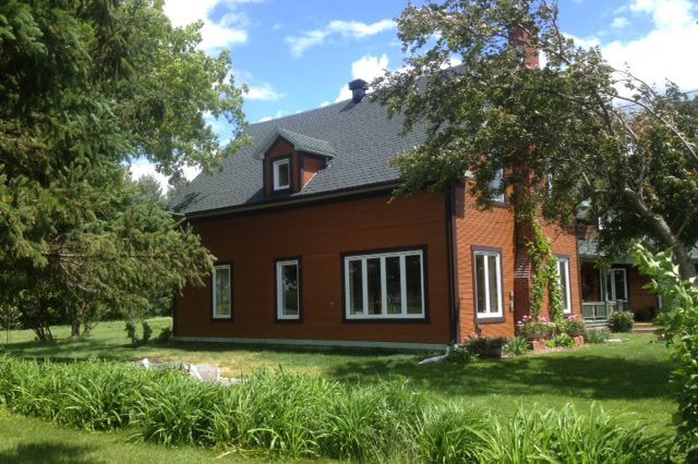 Une grande maison en briques rouges avec un toit noir est entourée d'arbres et d'herbe.