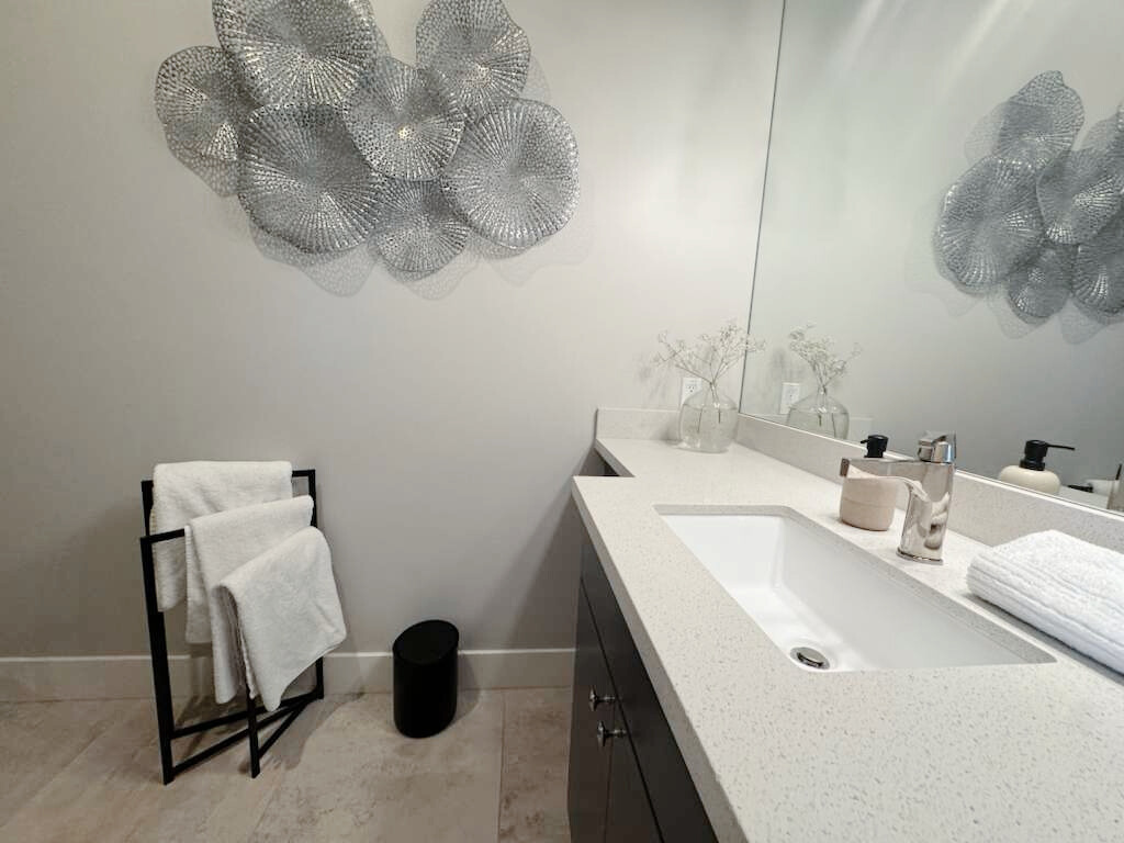 A modern bedroom featuring a bed with white bedding, a dark grey dresser under a television, and a window on the left.