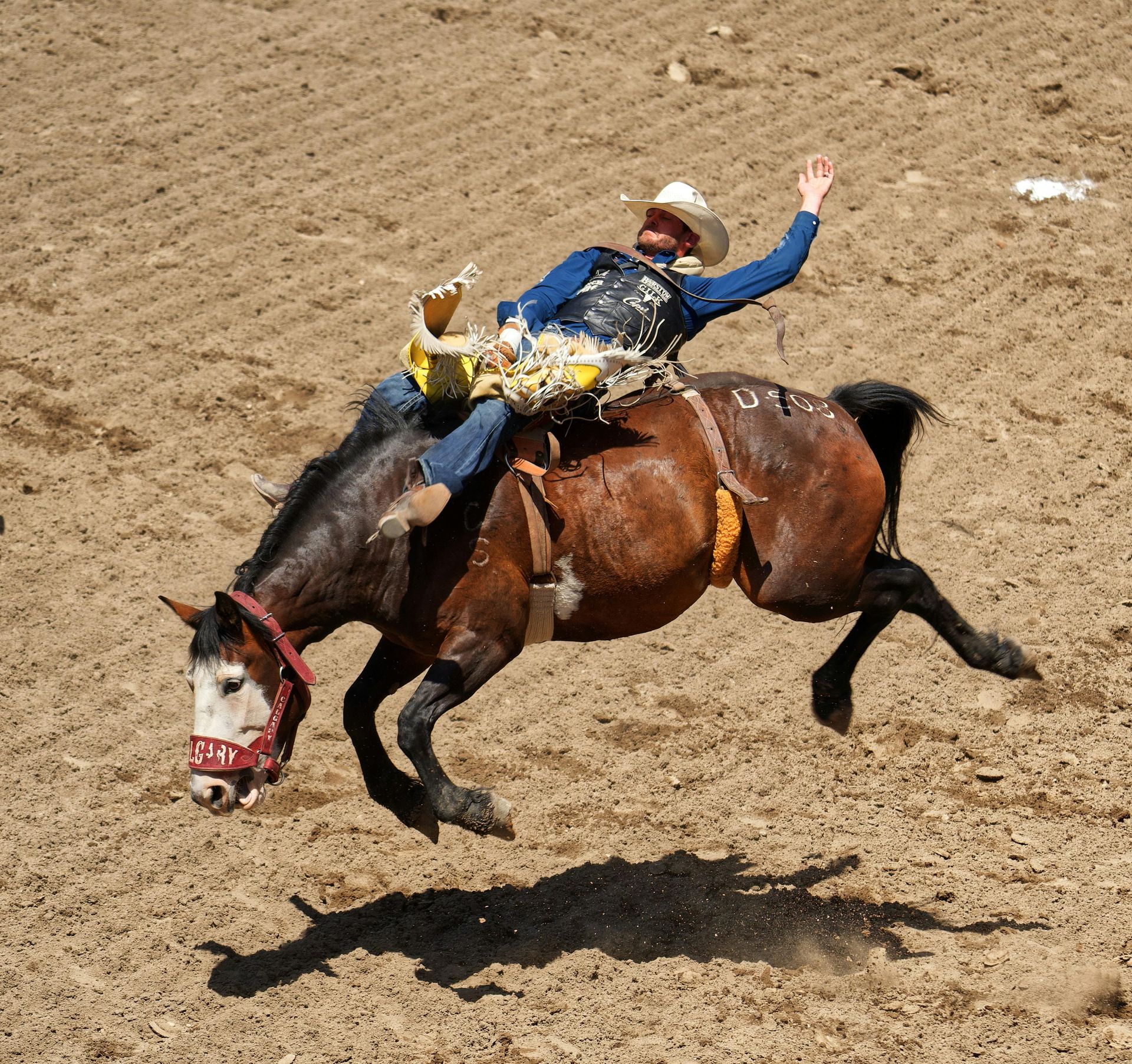A cowboy riding a bucking horse in a dirt arena.