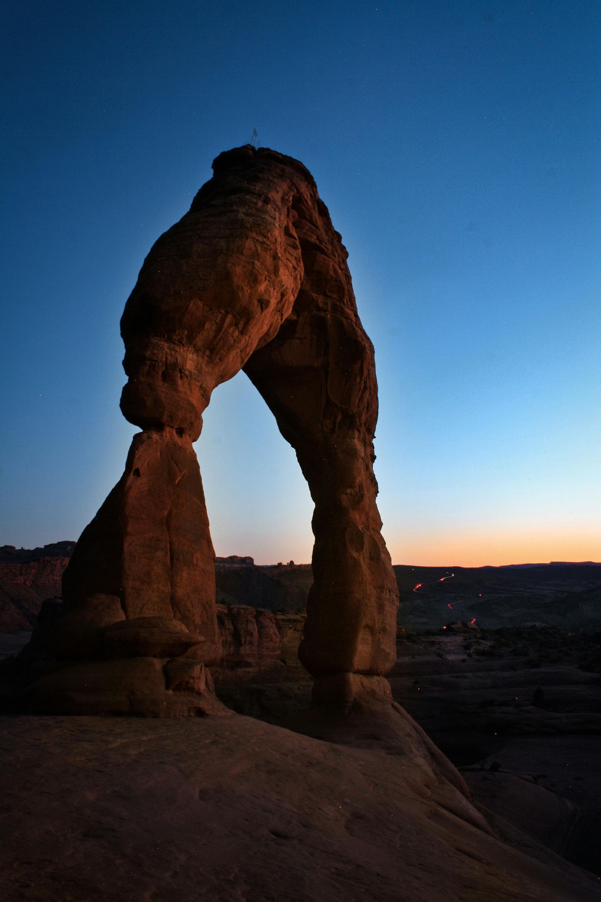 Delicate Arch in Arches National Park silhouetted against a deep blue dusk sky with a warm glow on the horizon.