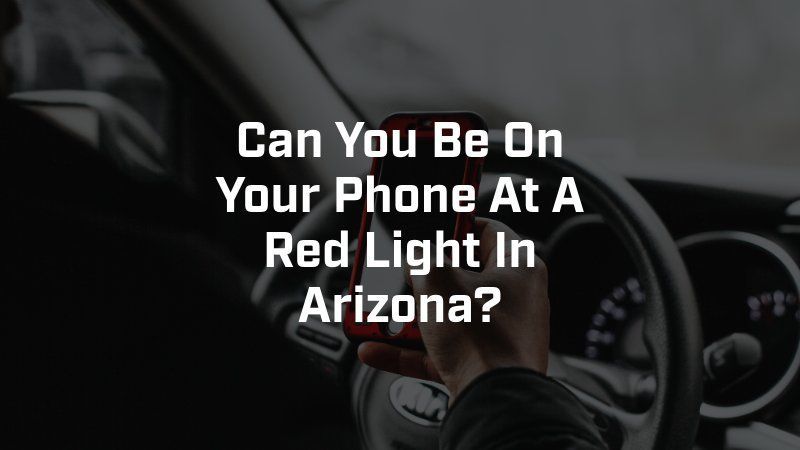 A person holding a cell phone in a car with the words can you be on your phone at a red light in arizona