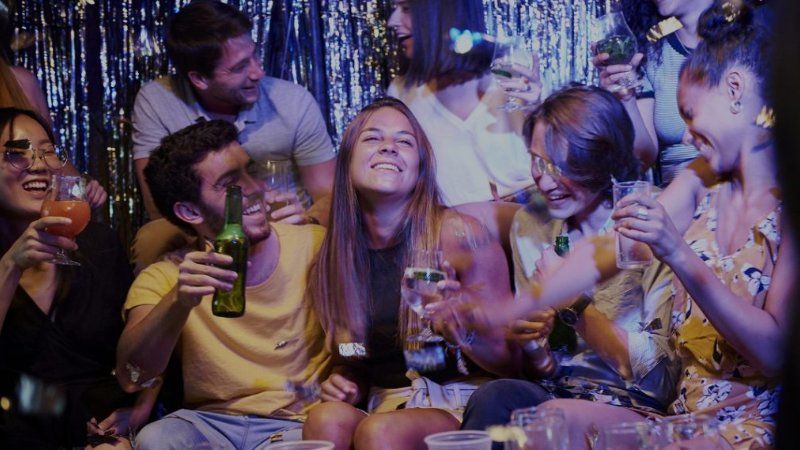 A group of people are sitting on the floor at a party holding drinks.