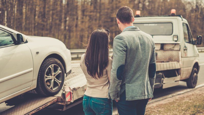 A man and a woman are standing next to a tow truck.