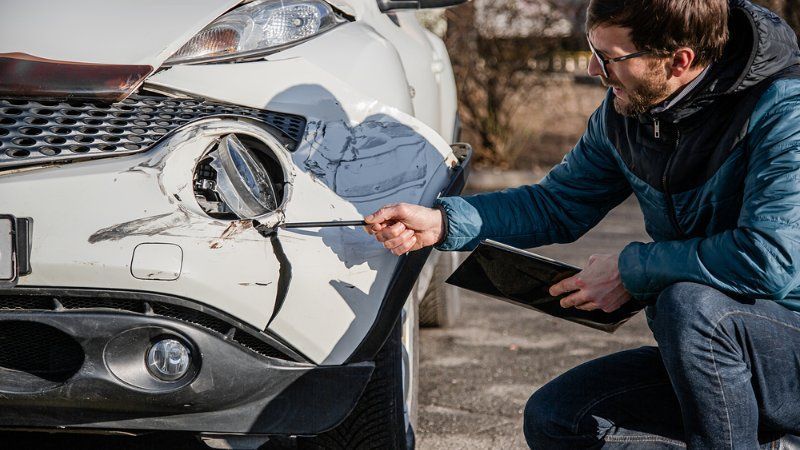 A man is kneeling down in front of a damaged car.