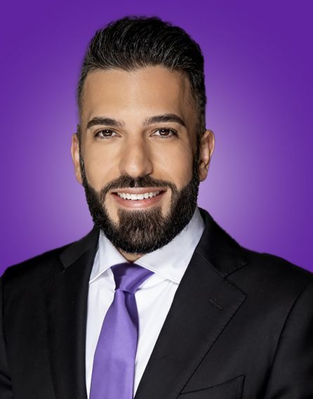 A man with a beard is wearing a black suit and purple tie.